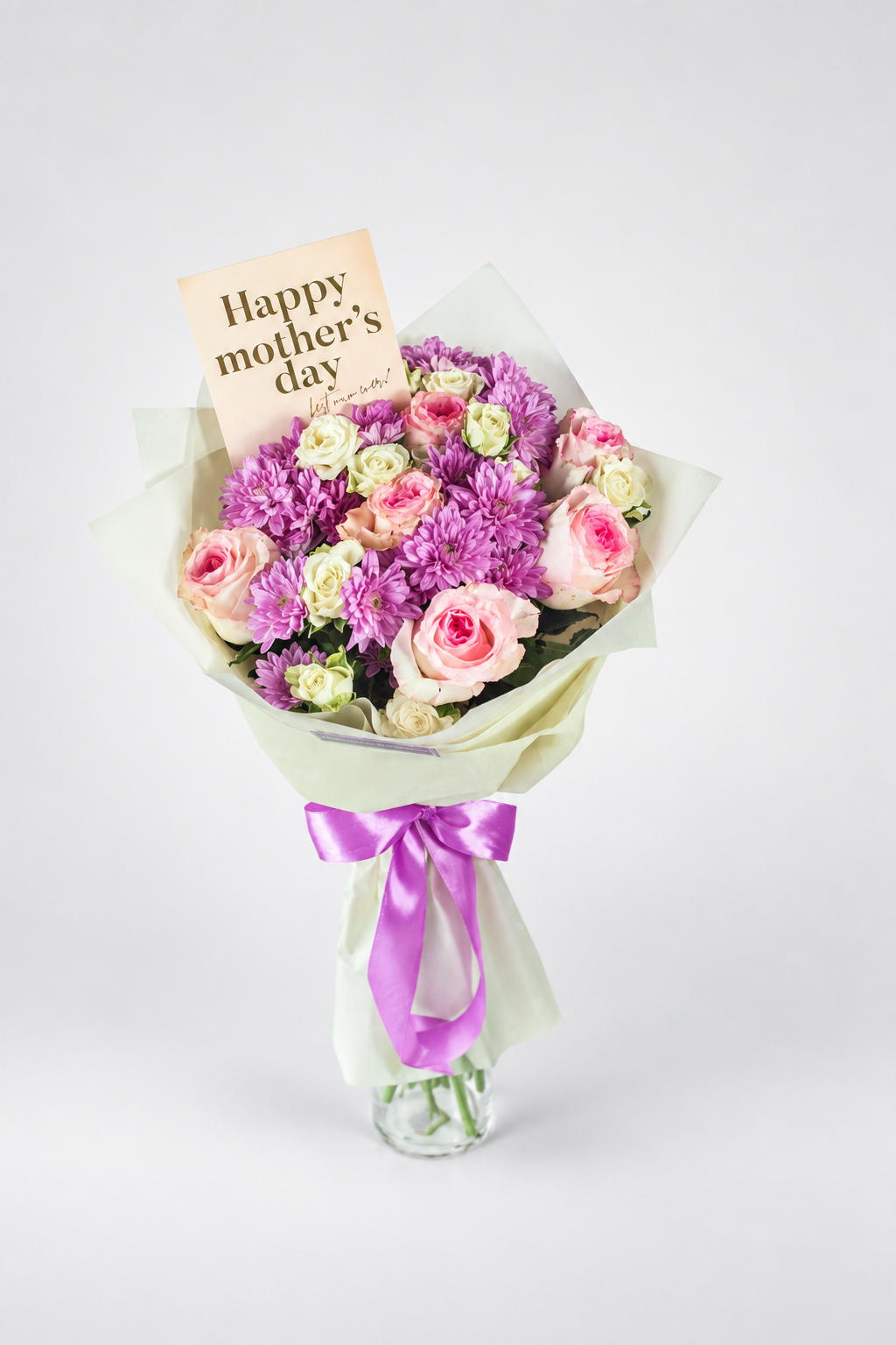 A fresh flower bouquet in a clear glass vase with a purple ribbon bow, featuring pink and purple roses, purple chrysanthemums, and a &