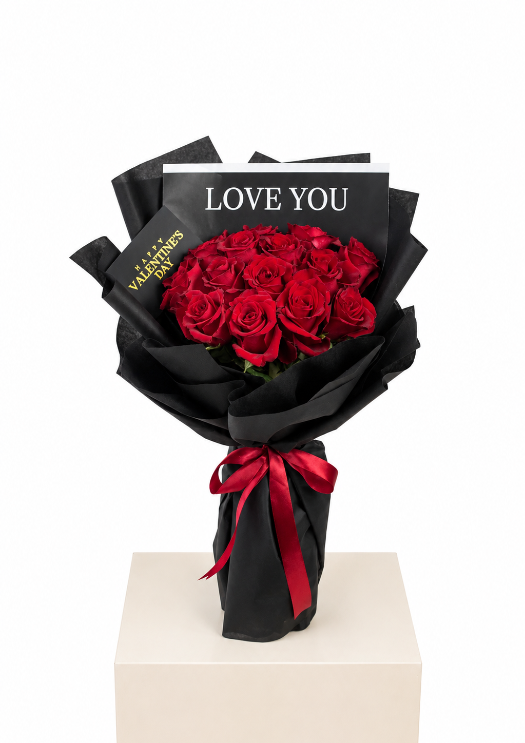 A bouquet of 15 red roses wrapped in black paper with a red ribbon and a card that reads &