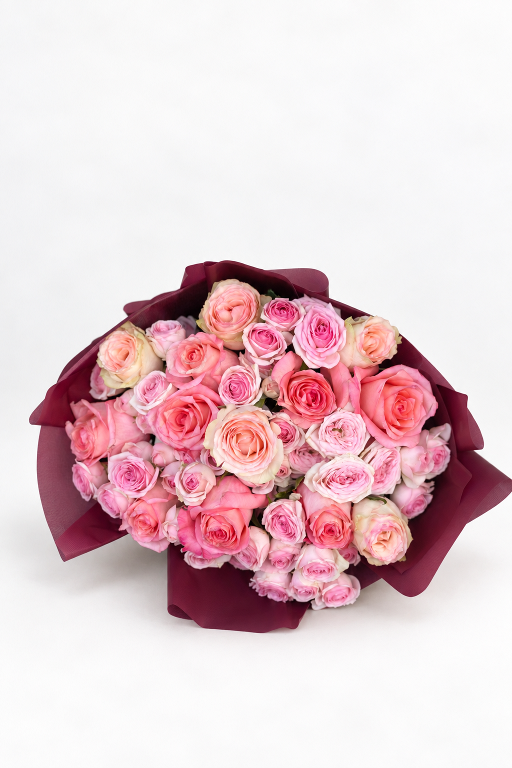 Rosie Rhapsody bouquet of pink, cream, and blush roses wrapped in maroon paper with a pink ribbon and card