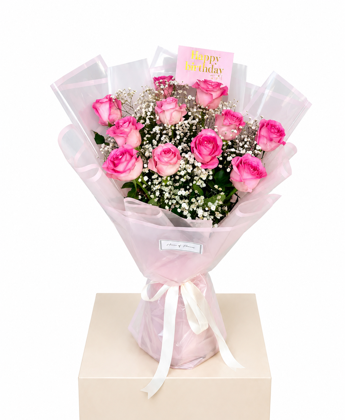 A bouquet of pink roses wrapped in sheer light pink paper with a white ribbon.