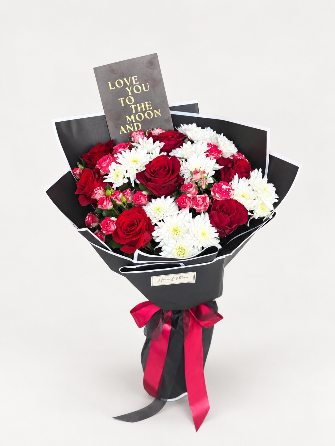 Dusky Romance bouquet of red roses, pink carnations, and white chrysanthemums wrapped in black paper with a red ribbon and a "Love You to the Moon" card
