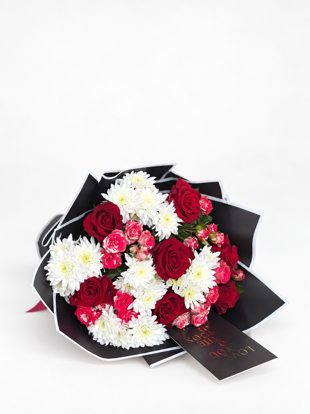 Dusky Romance bouquet of red roses, pink carnations, and white chrysanthemums wrapped in black paper with a red ribbon and a "Love You to the Moon" card