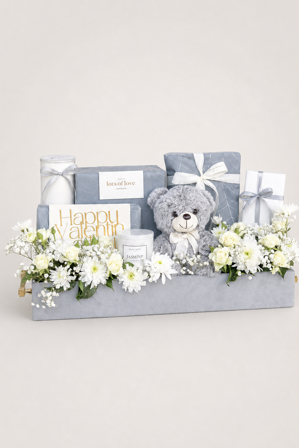 Grey gift box hamper with white flowers, plush teddy bear, and wrapped gifts.