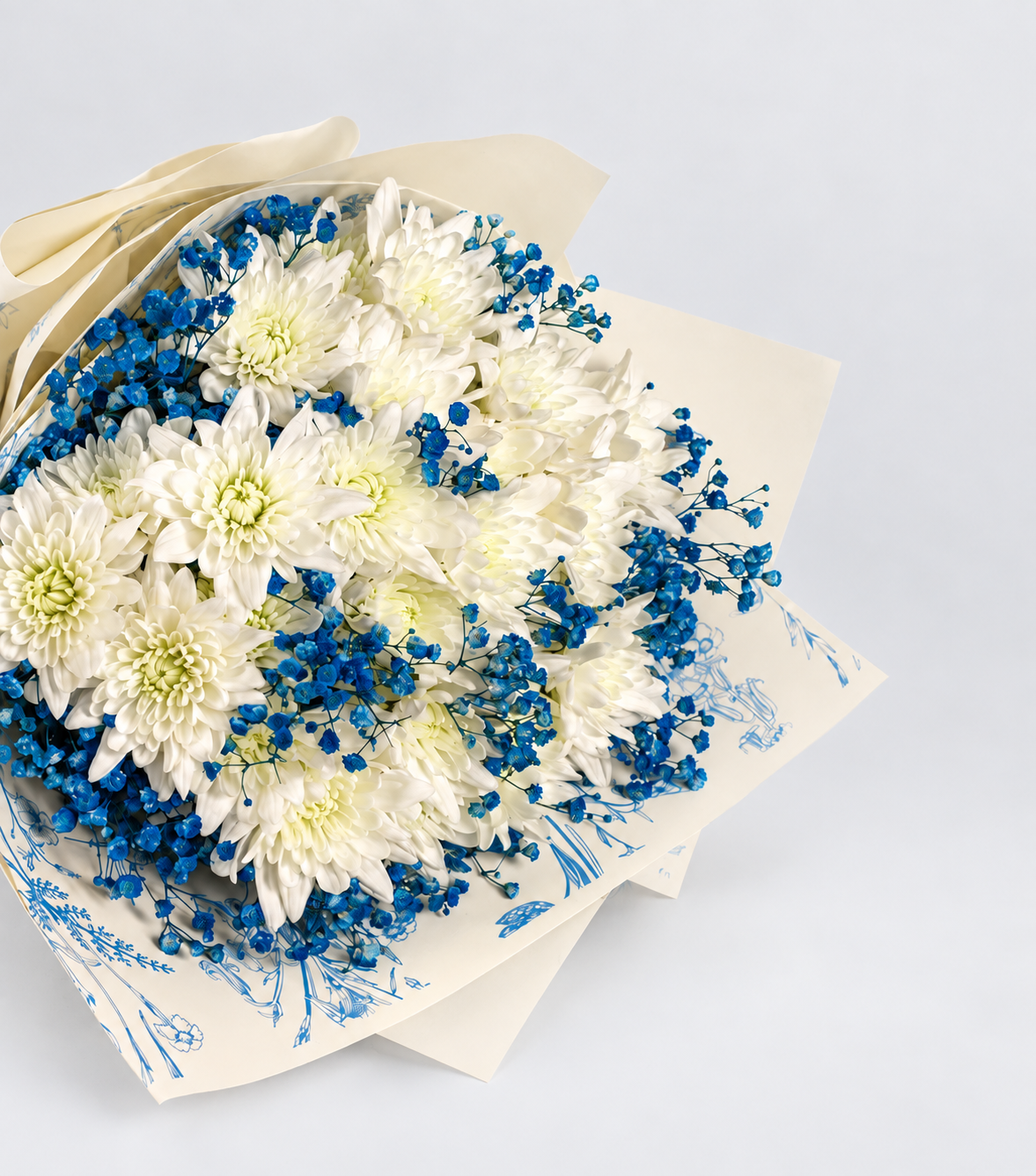A bouquet of white and blue flowers wrapped in white paper with a blue botanical pattern and tied with a dark blue ribbon, displayed on a white pedestal against a white background.