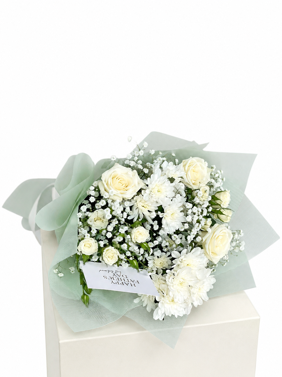 A bouquet of white and pale yellow flowers wrapped in sheer pale green paper, displayed on top of a white box against a white background.