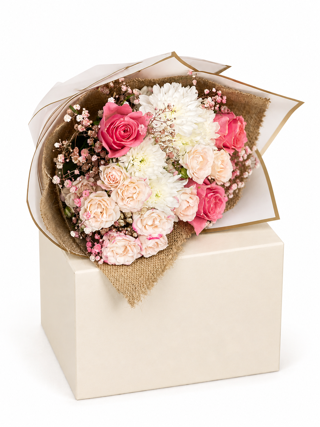 A floral bouquet with pink and white flowers wrapped in beige paper and burlap, displayed on top of a cream gift box against a white background.
