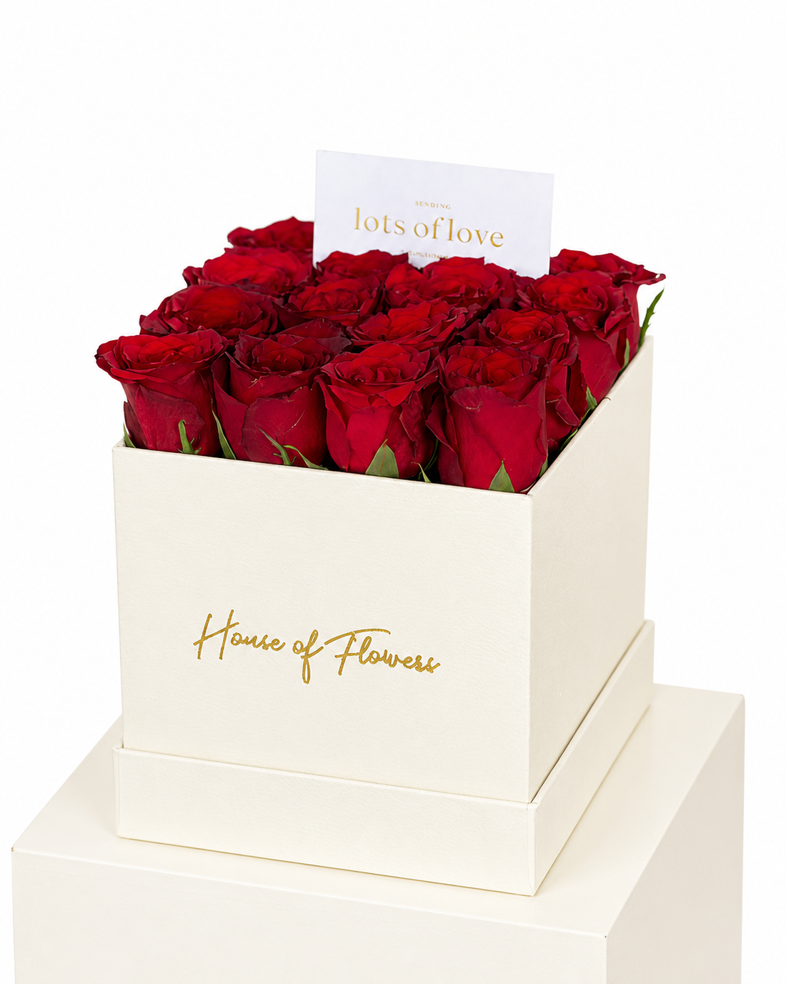 A premium gift box of red roses from House of Flowers, featuring a stack of two cream-colored square boxes with gold foil branding, filled with vibrant red roses and topped with a white card that reads &