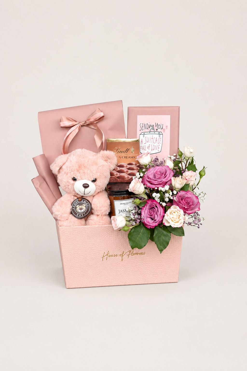 Rosy Plum gift box with pink and purple roses, a teddy bear, chocolates, and a candle in a blush pink box.