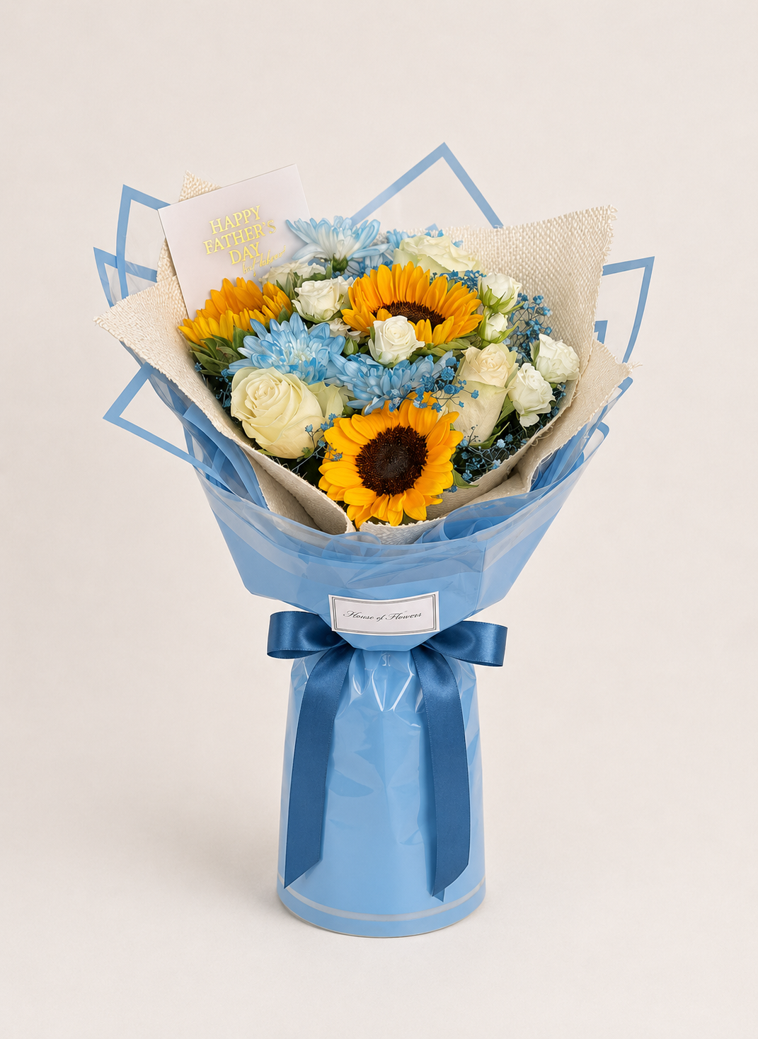 A wrapped flower bouquet featuring yellow sunflowers, white roses, and blue flowers, wrapped in light blue paper with a matching blue ribbon bow, set against a plain light beige background.