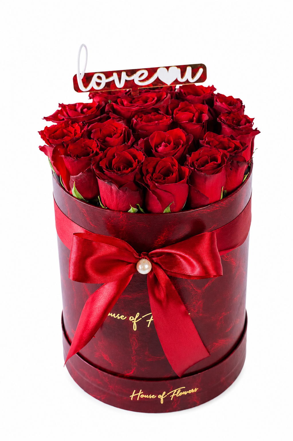 A round gift box filled with deep red roses, wrapped in a matching dark red ribbon with a pearl accent and gold script lettering. A small &