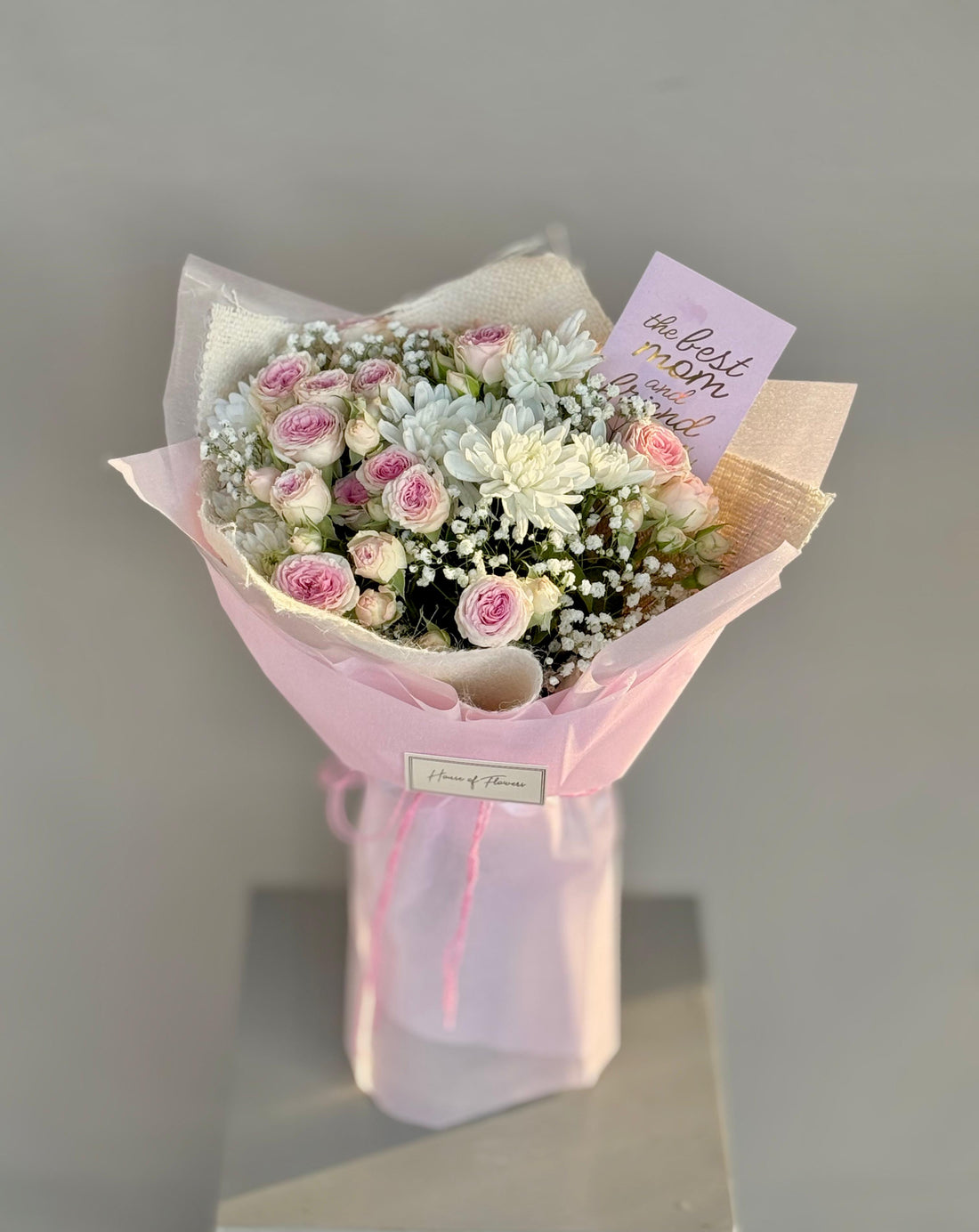 Bouquet of flowers wrapped in pink paper with a card on a gray background