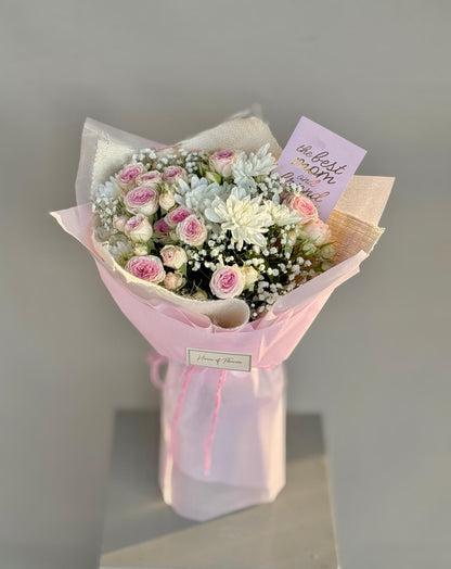 Bouquet of flowers wrapped in pink paper with a card on a gray background
