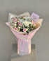 Bouquet of flowers wrapped in pink paper with a card on a gray background