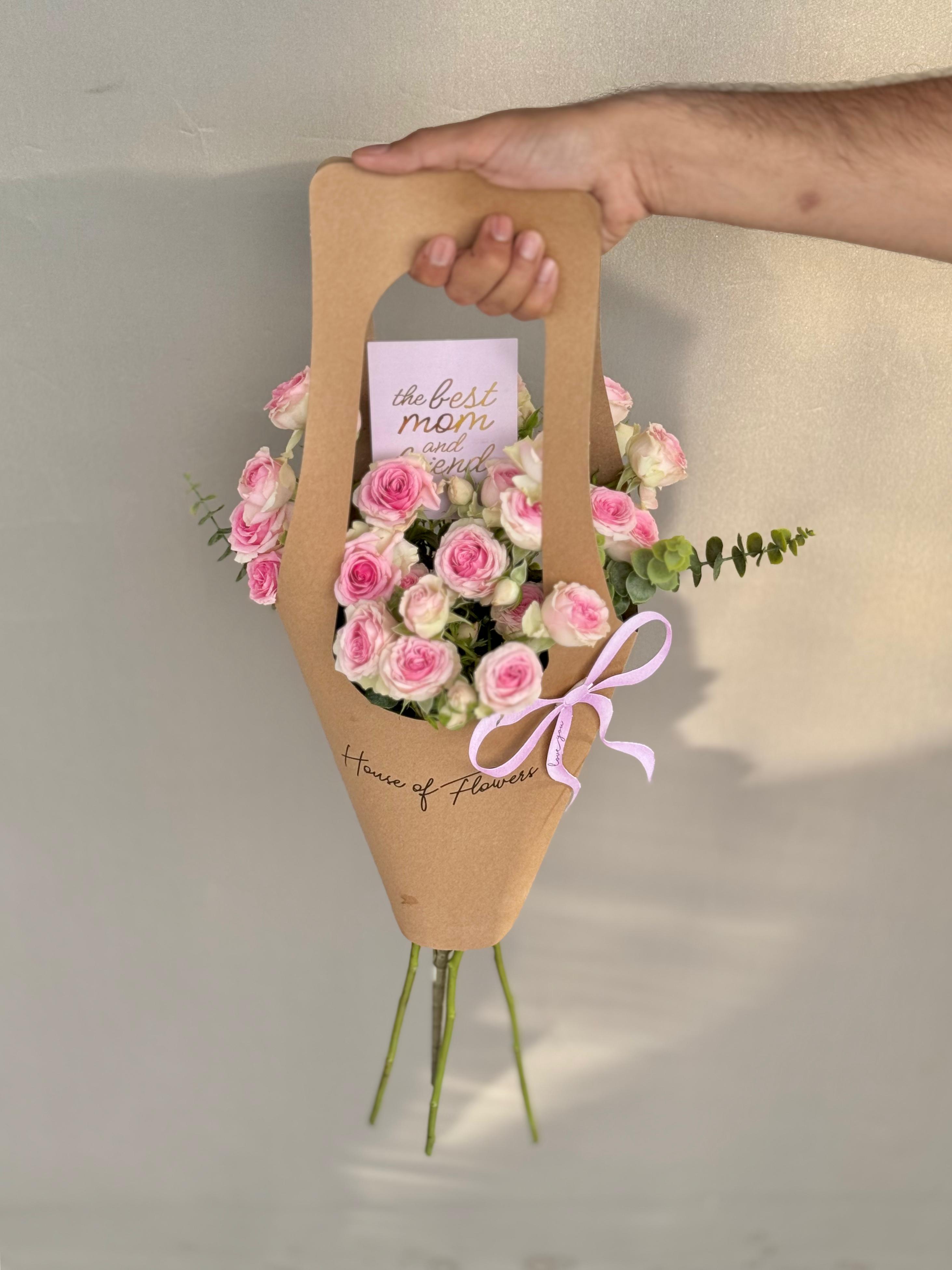 Purely for Her bouquet with pink roses in a kraft paper carrier bag with a "The Best Mom" card and pink ribbon