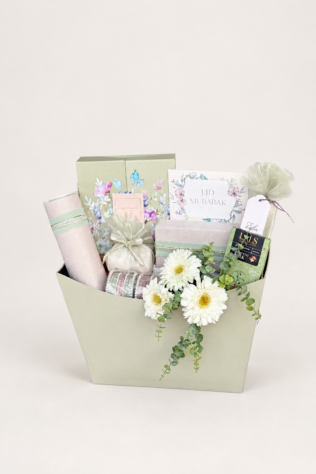 Light sage green hamper box filled with white gerbera daisies, wrapped mithai, Pringles, bangles, Lals chocolate bar, and greeting cards.