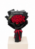 A bouquet of 15 red roses wrapped in black paper with a red ribbon and a card that reads &