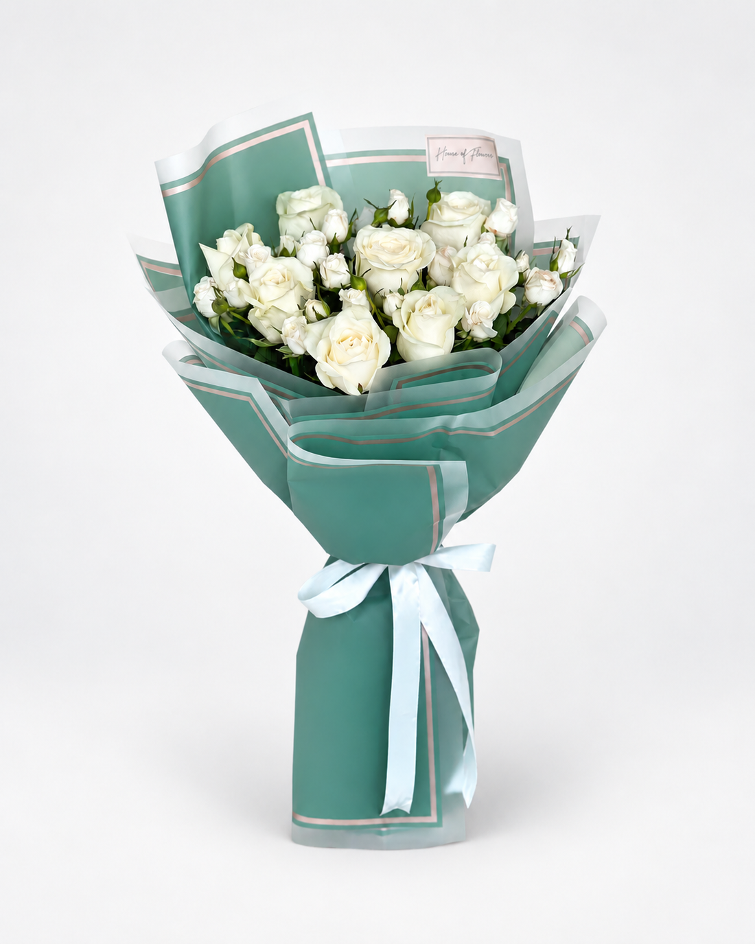 A bouquet of white roses wrapped in teal-green paper with thin gold borders and tied with a pale blue ribbon, photographed on a clean white background.