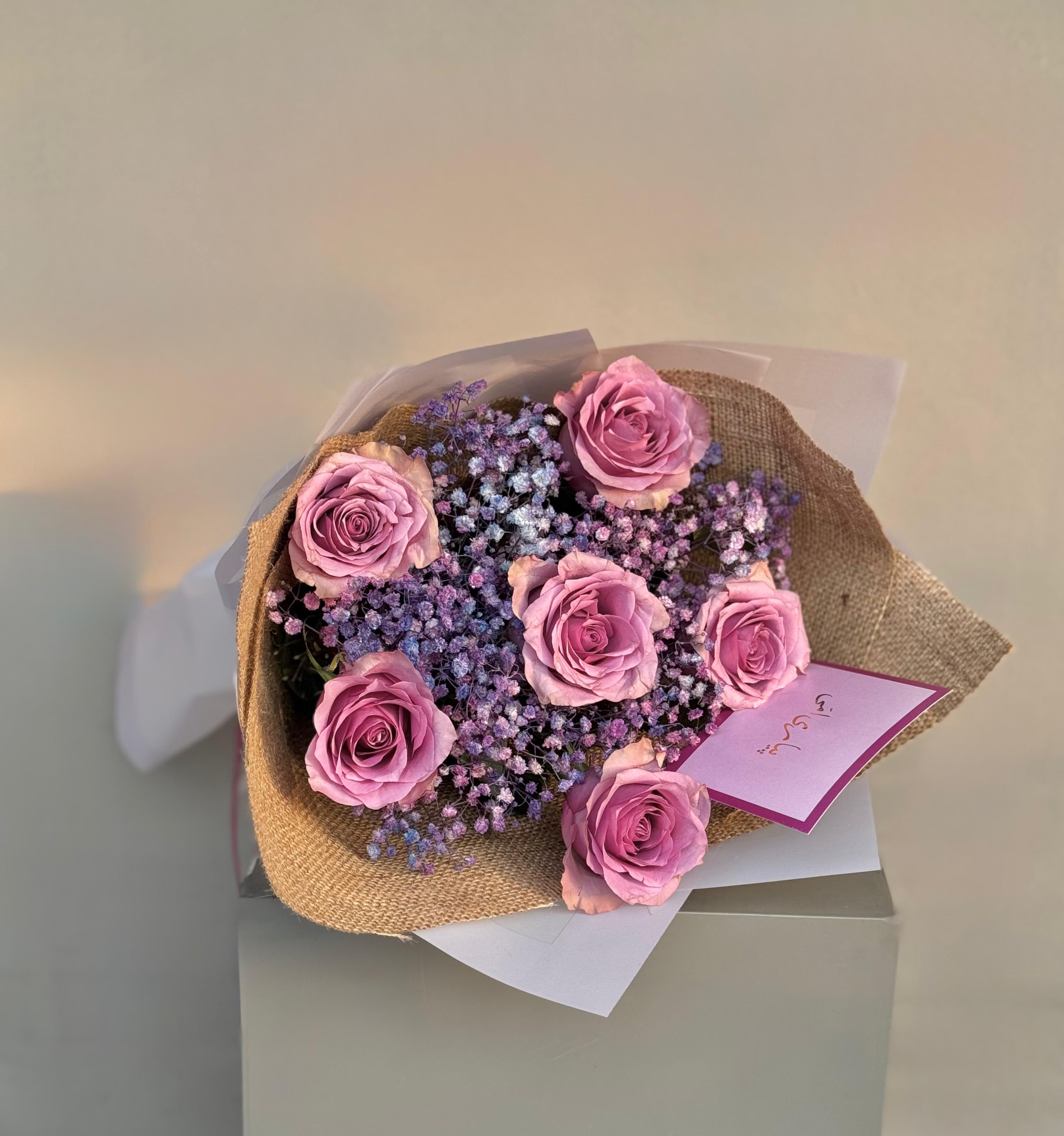Bouquet of pink roses and purple flowers with a card on a light background