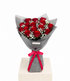 A bouquet of 12 red roses wrapped in gray paper with a bright red ribbon bow, displayed on a white pedestal against a white background.