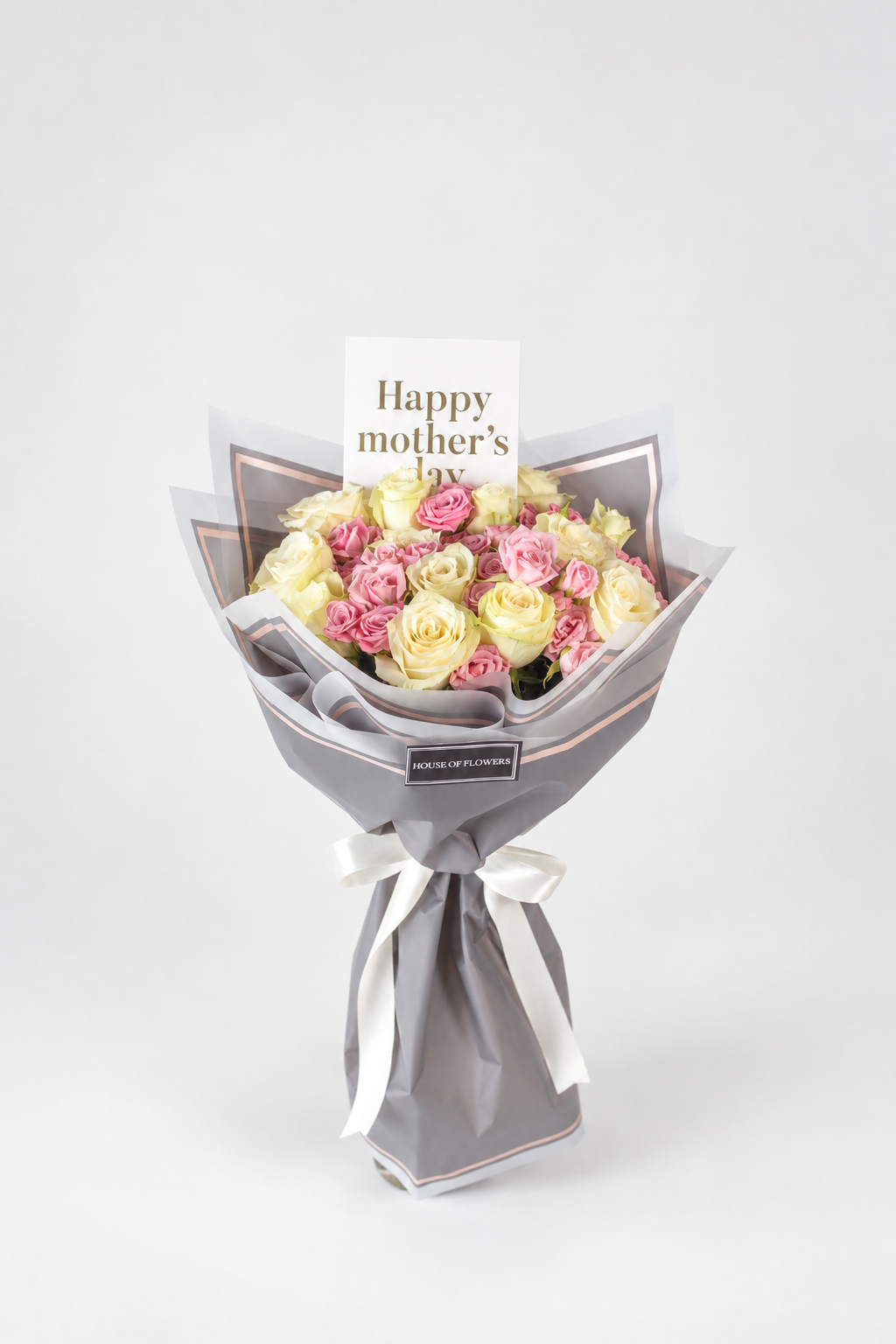 A bouquet of yellow and pink roses wrapped in gray paper with a white ribbon and a small card that reads &