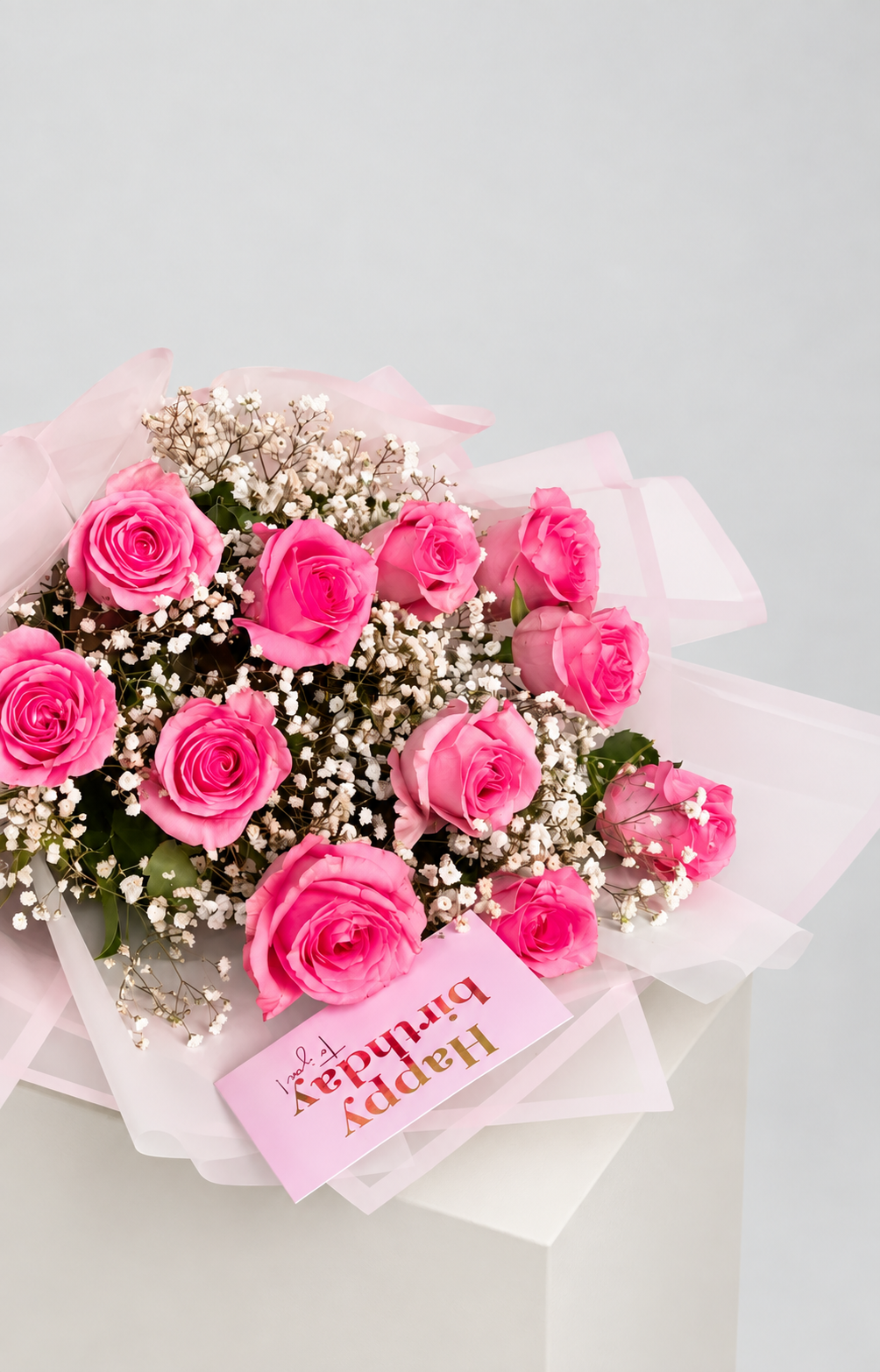 A bouquet of pink roses wrapped in sheer light pink paper with a white ribbon. 