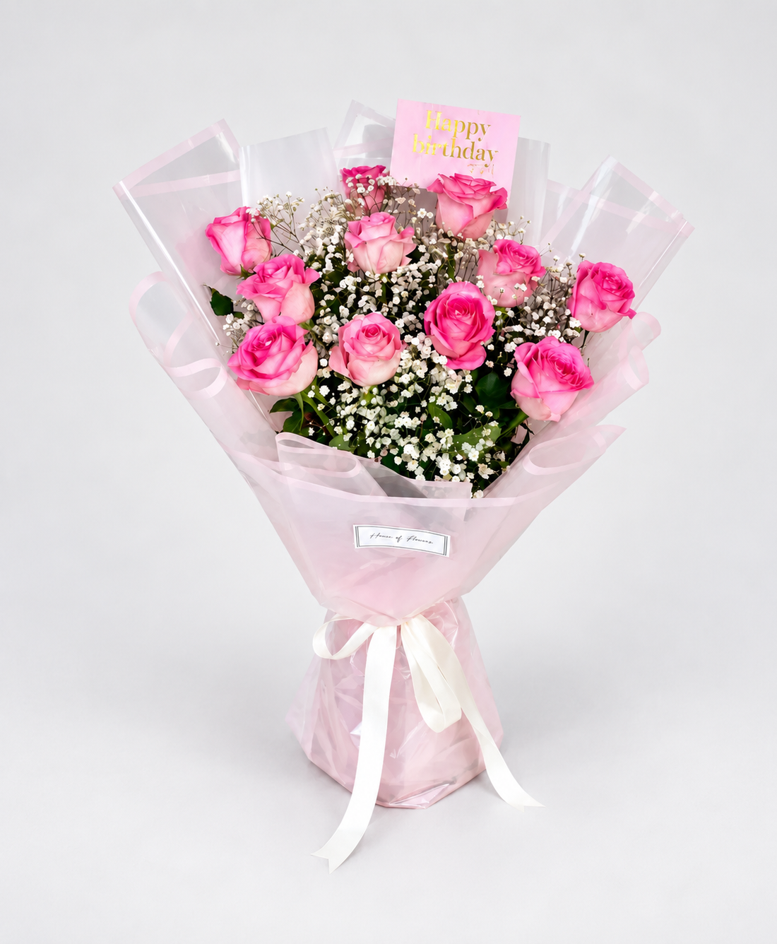 A bouquet of pink roses wrapped in sheer light pink paper with a white ribbon. 