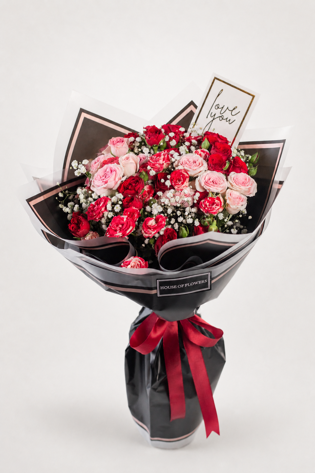 A floral bouquet wrapped in black paper with a red ribbon, featuring pink and red roses, baby&