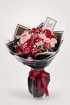 A floral bouquet wrapped in black paper with a red ribbon, featuring pink and red roses, baby&