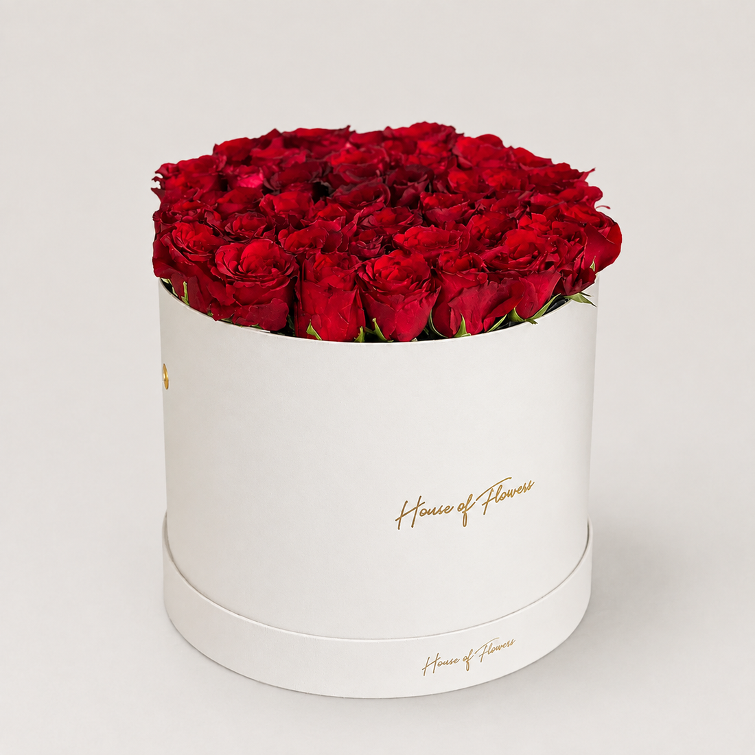 A bouquet of red roses with green eucalyptus stems arranged in a white cylindrical box printed with the gold script &