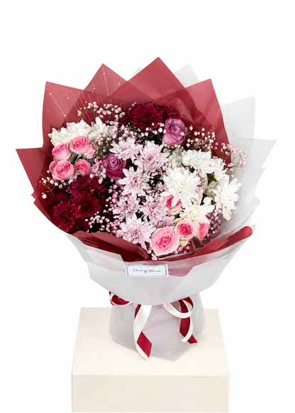 A floral bouquet with pink and burgundy roses, white and pink daisies, and baby&