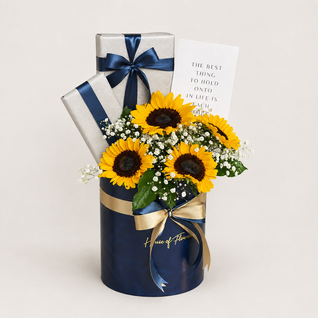 A gift arrangement in a navy blue cylindrical box from Home of Flowers, featuring yellow sunflowers, white baby&