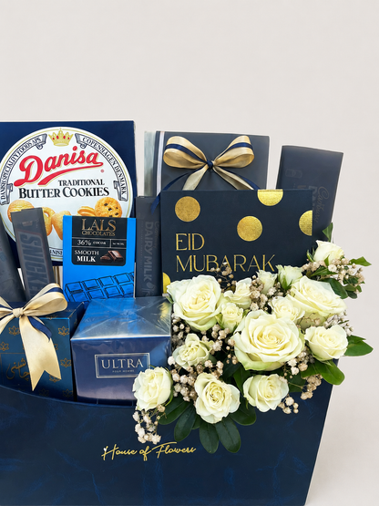 House of Flowers Eid Treats gift box with Danisa Butter Cookies, Lals Chocolates, Cadbury, J. ULTRA perfume, Mithai, and fresh white roses with gypsophila in a navy blue branded box