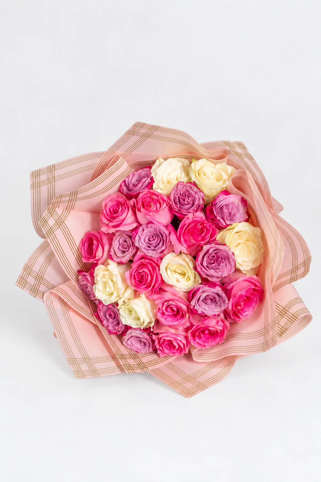 A bouquet of fresh roses, featuring a mix of pink, purple, and white roses, wrapped in yellow and clear paper with a pink ribbon.