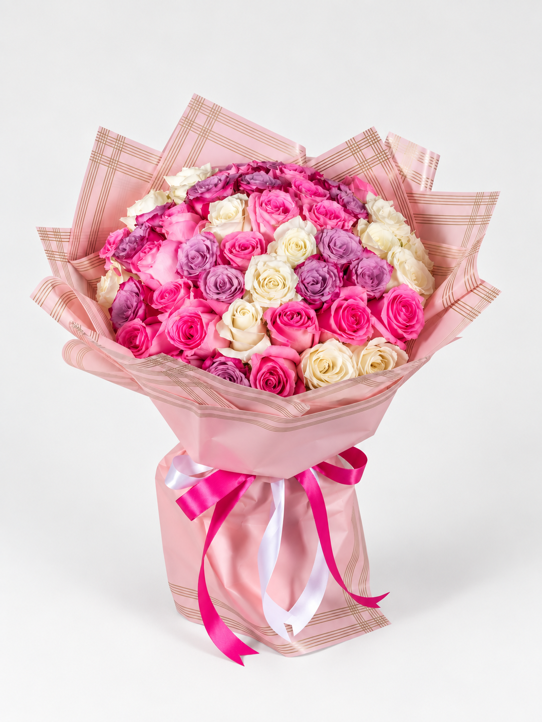 A bouquet of fresh roses, featuring a mix of pink, purple, and white roses, wrapped in yellow and clear paper with a pink ribbon.