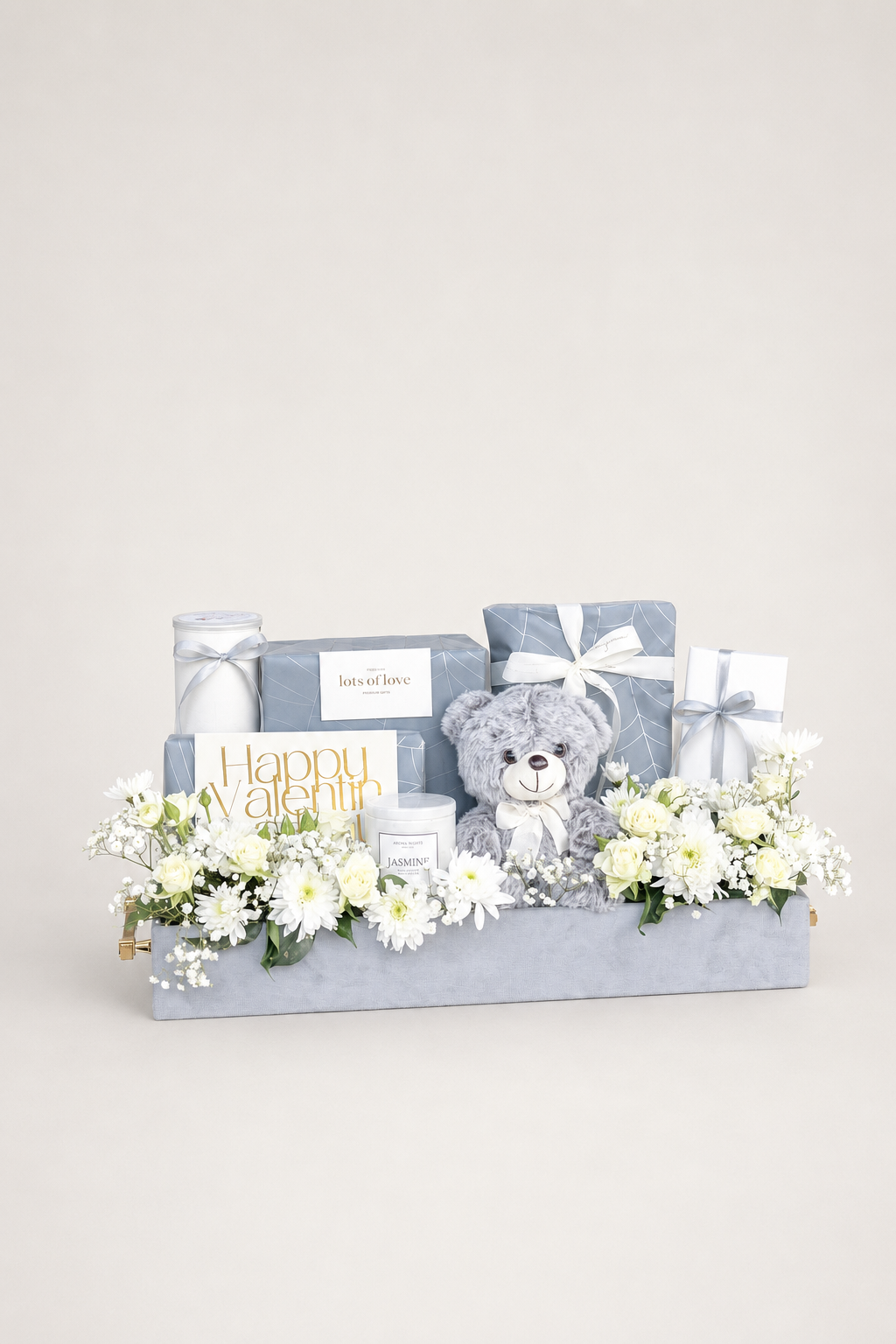 Grey gift box hamper with white flowers, plush teddy bear, and wrapped gifts.