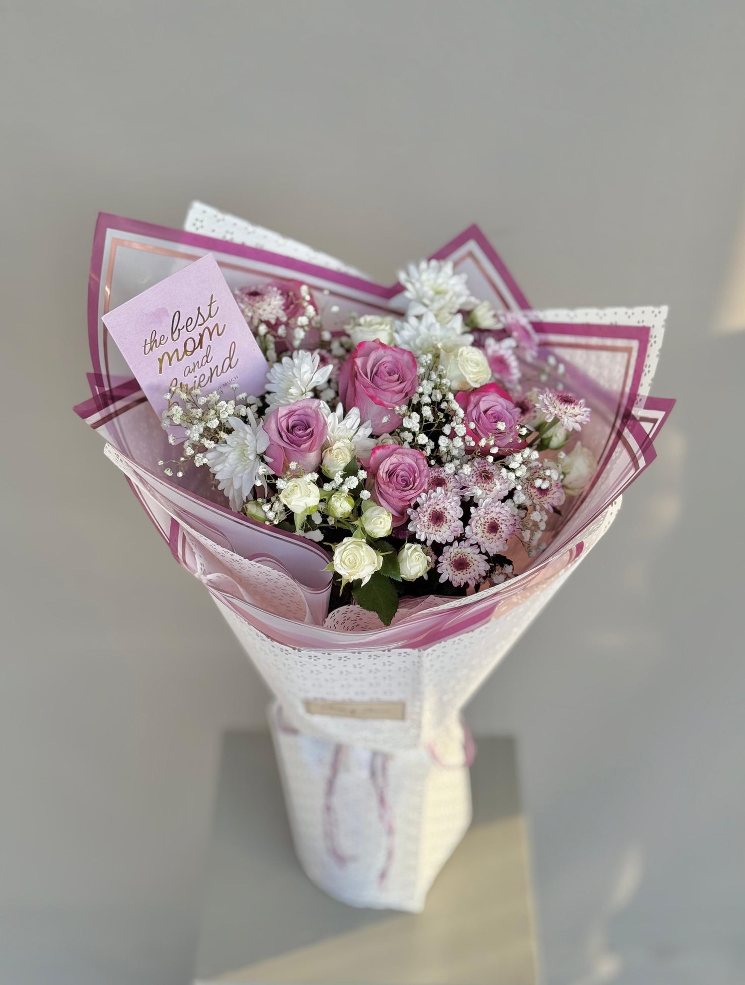 Eternal Maternal bouquet with pink and white roses and white chrysanthemums, wrapped in patterned pink paper with a "Best Mom" card