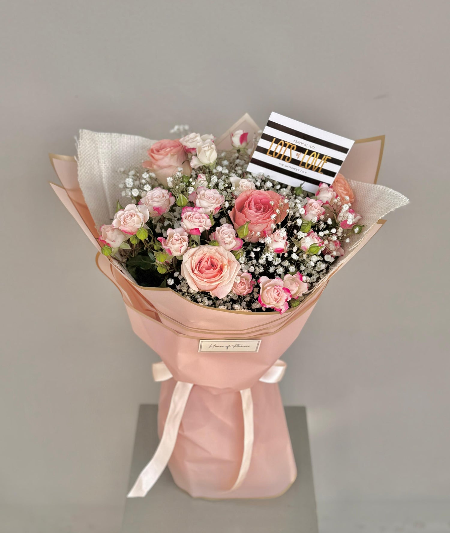 Bouquet of pink flowers wrapped in pink paper with a gray background