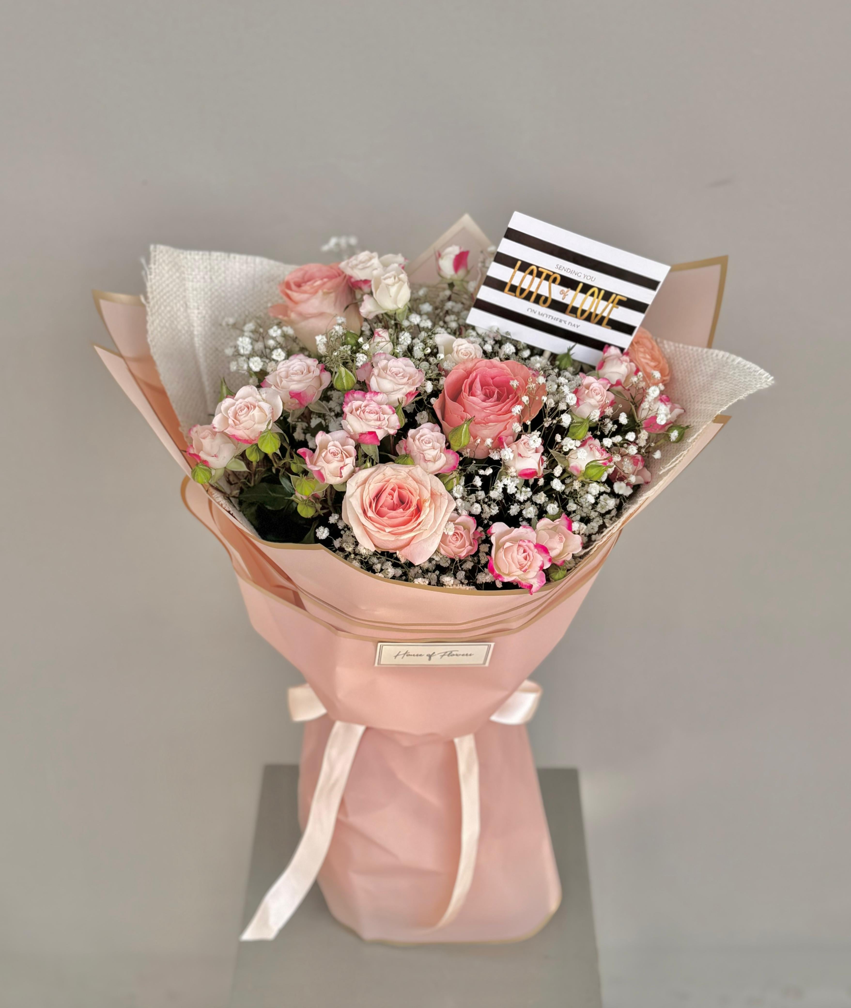 Bouquet of pink flowers wrapped in pink paper with a gray background