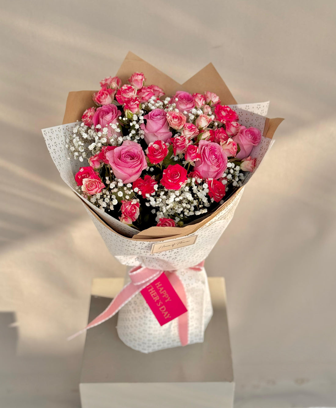 Bouquet of pink roses with a white ribbon and card on a neutral background