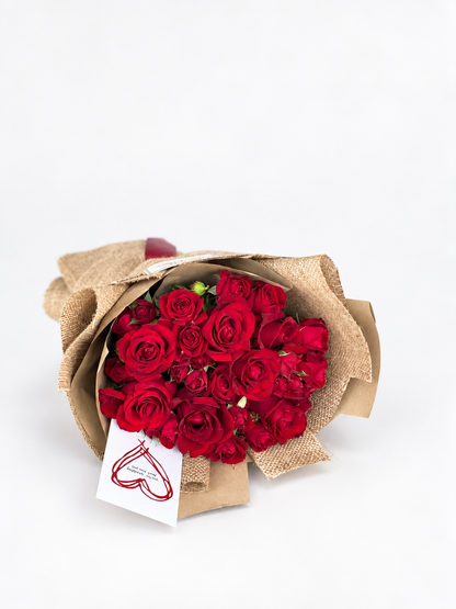 Forbidden Rose bouquet of red roses wrapped in beige burlap paper with a red ribbon and a heart-drawn card