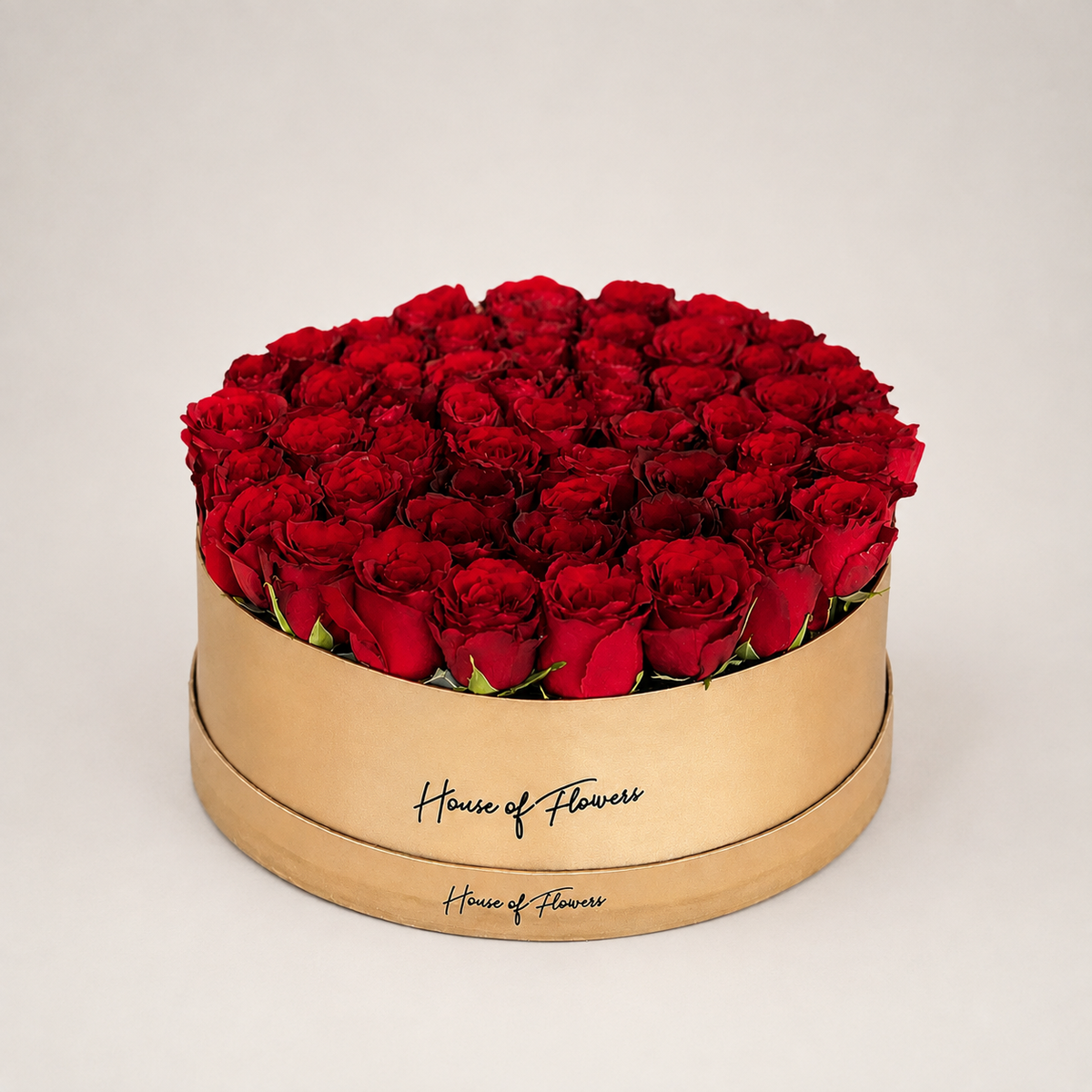 A round gift box filled with red roses, featuring a gold-colored wooden base printed with the brand name &