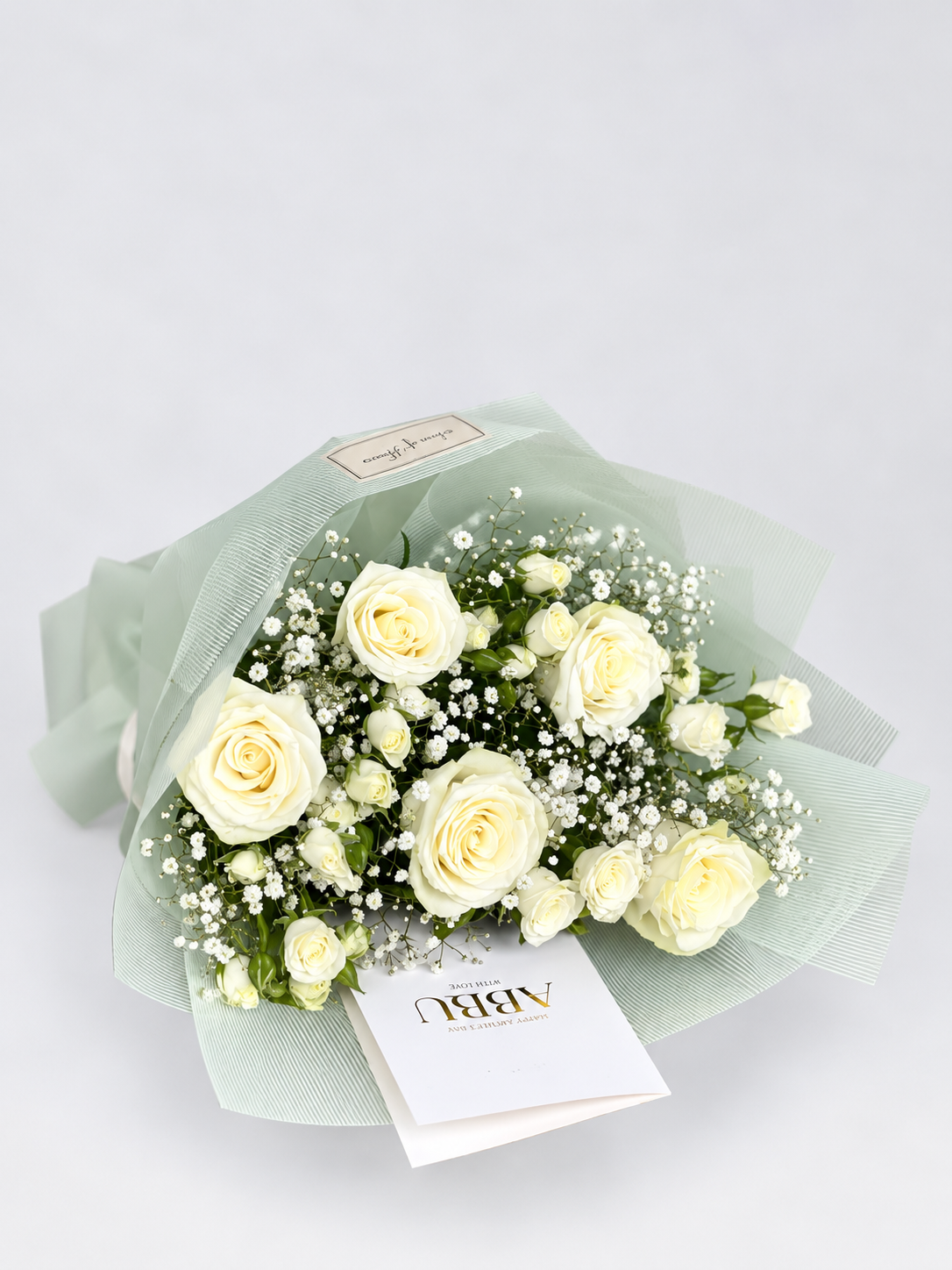 His Arms bouquet with white roses and gypsophila, wrapped in mint green paper with a white ribbon and an "Abbu" card