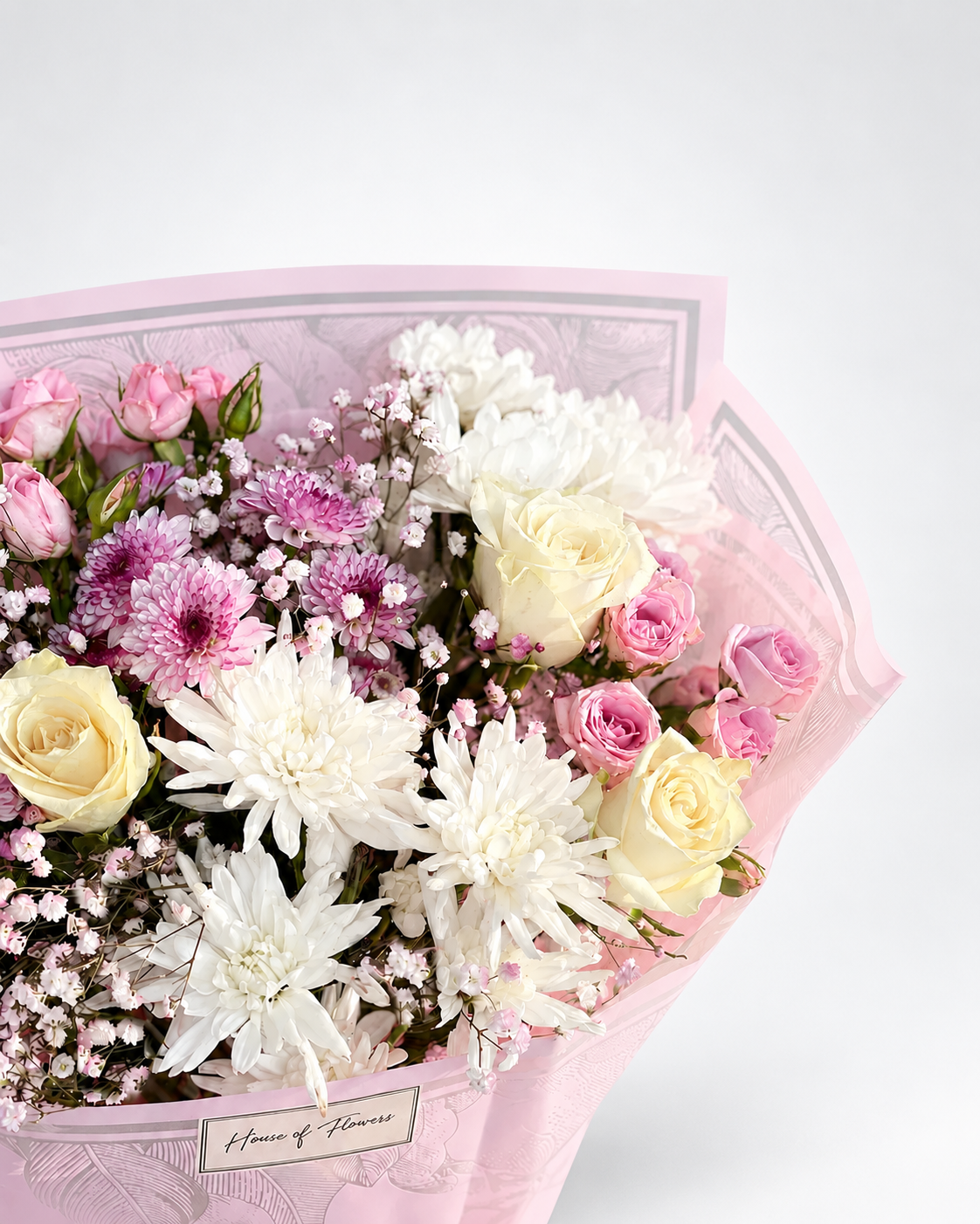 A floral bouquet wrapped in light pink paper, featuring white and pink roses, white chrysanthemums, pink chrysanthemums, and baby&