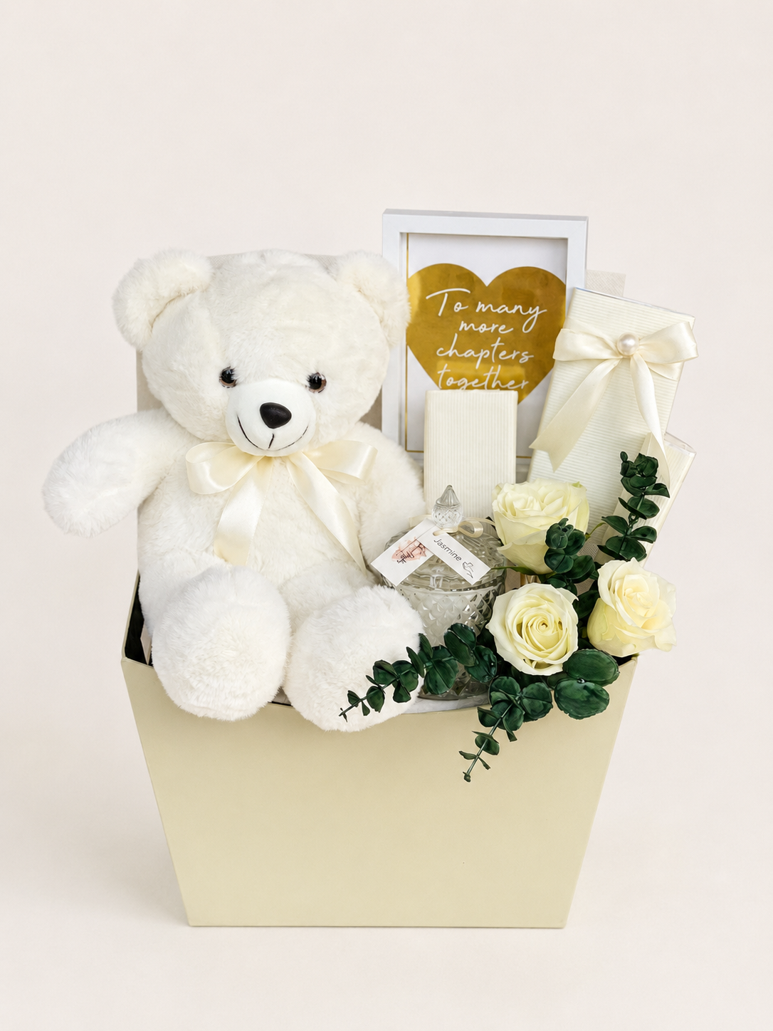 Love &amp; Lullabies cream gift box by House of Flowers featuring a white teddy bear with satin bow, white roses, eucalyptus, jasmine candle jar, ribbon-wrapped gift, and "To Many More Chapters Together" framed print