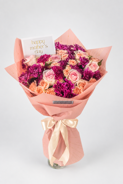 A vibrant bouquet of roses and carnations wrapped in peach paper with a satin ribbon, featuring a &