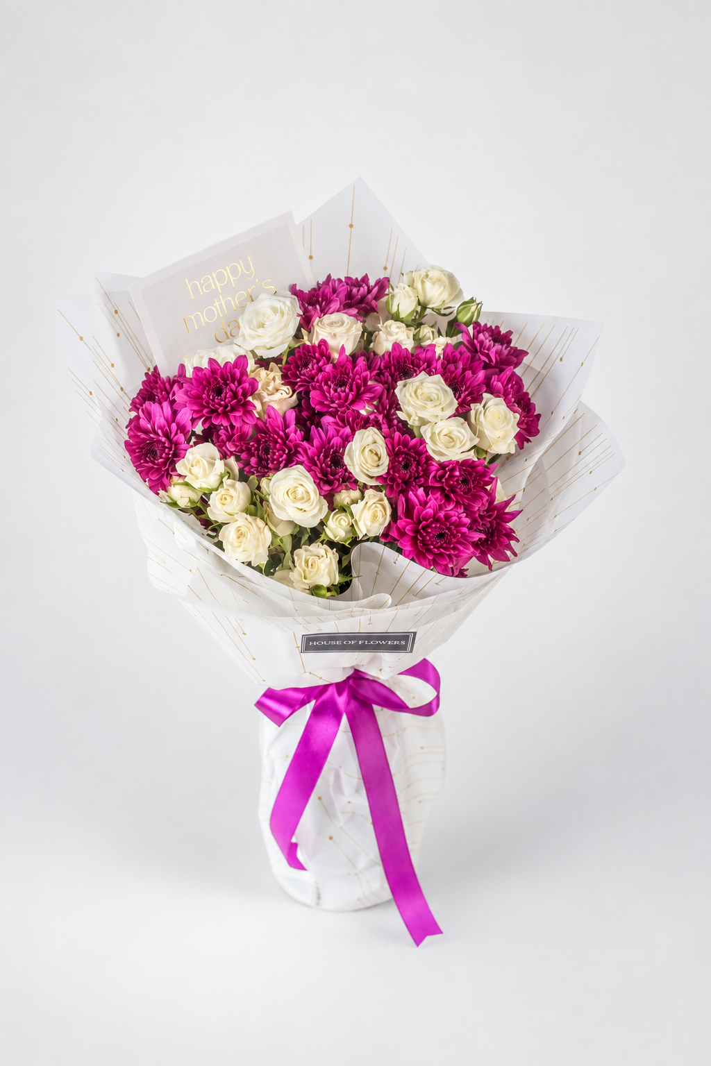 A floral bouquet wrapped in white royal premium sheet with gold speckles, featuring a mix of deep magenta chrysanthemums and cream roses, tied with a bright pink ribbon at the base.