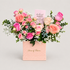 A floral gift arrangement in a pink box from House of Flowers, featuring pink and peach roses, green foliage, small white flowers, blue berries, and a card that reads &