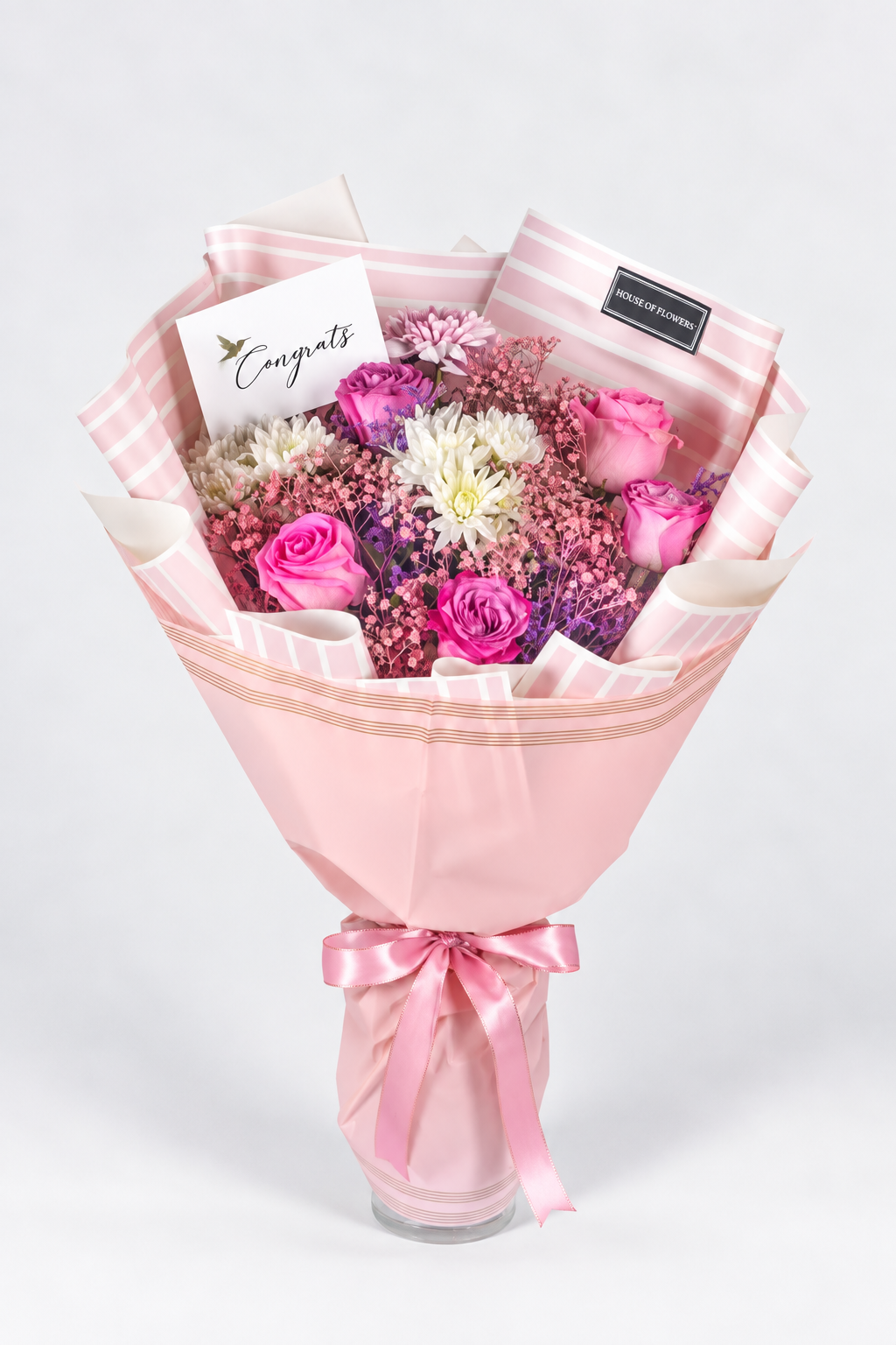 A bouquet of flowers including roses and chrysanthemums in purple, pink, and white colors, with a pink veil wrapped around the stems, tied with a pink ribbon.