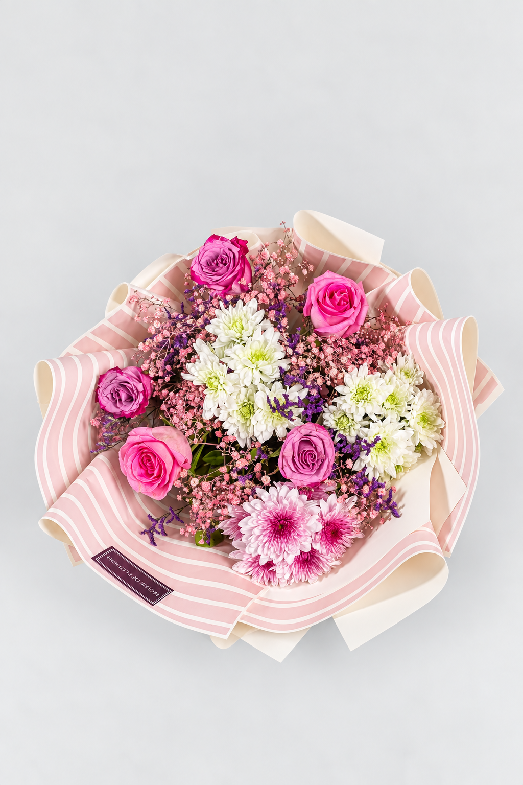 A bouquet of flowers including roses and chrysanthemums in purple, pink, and white colors, with a pink veil wrapped around the stems, tied with a pink ribbon.