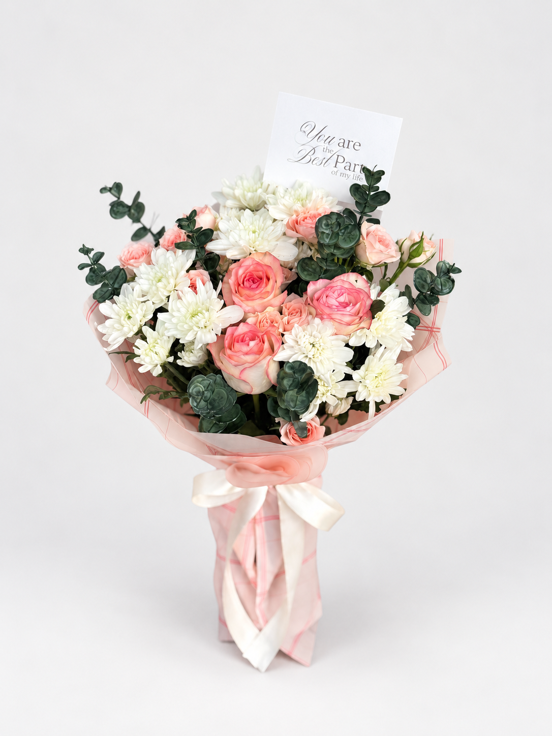 A floral bouquet with pink and white flowers, green foliage, and a small card that reads &
